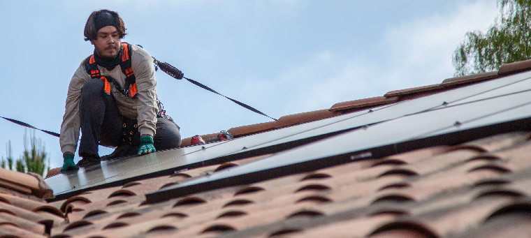 Installer setting solar panel in place on clay tile roof.