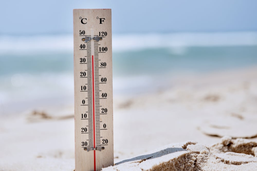 Thermometer sticking out of the sand at beach with high temperatures
